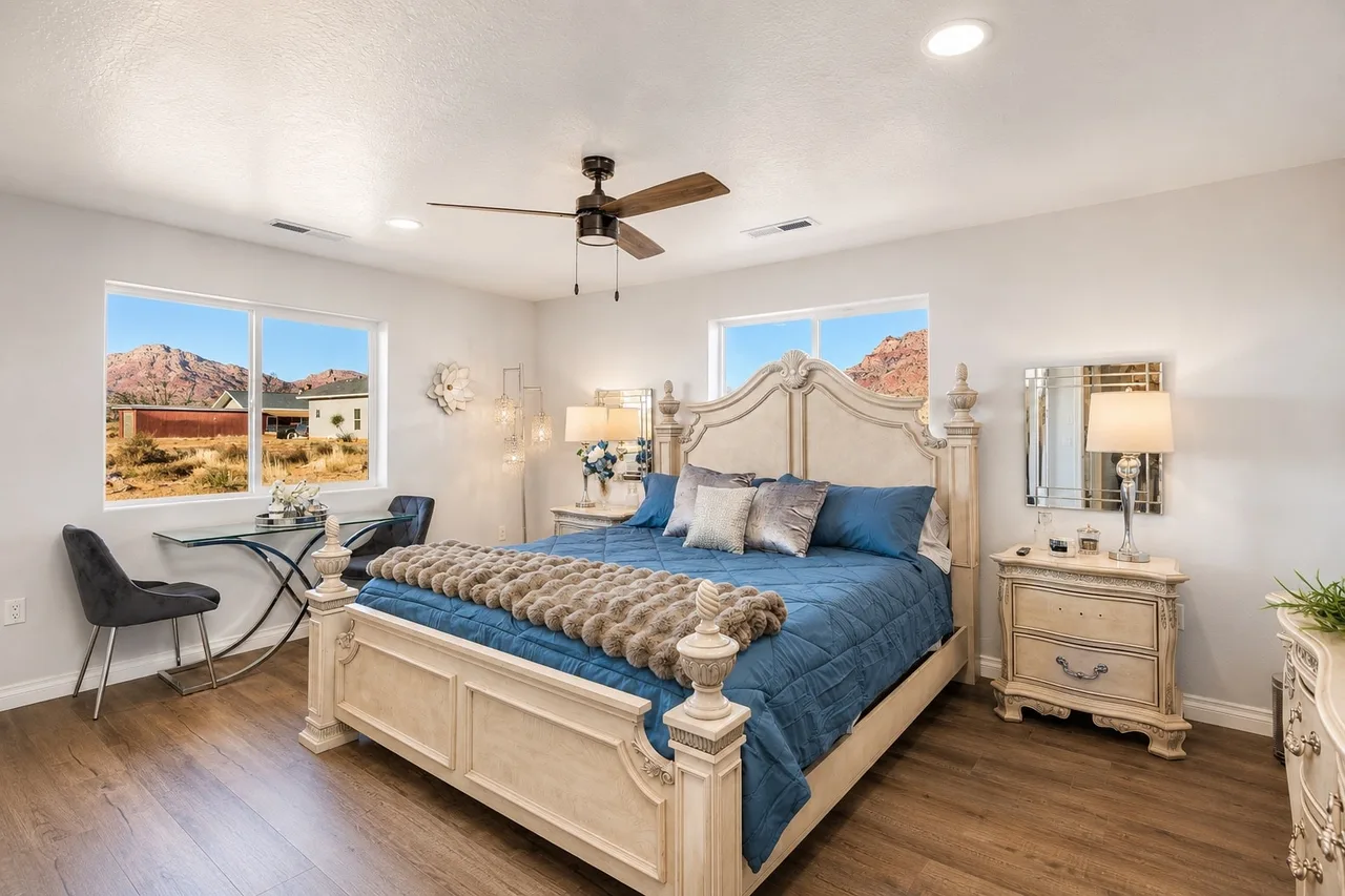 Ornate king bedroom in the Garden Suite with a cream heirloom headboard, blue quilted linens, glass writing desk, and a window onto the red cliffs.